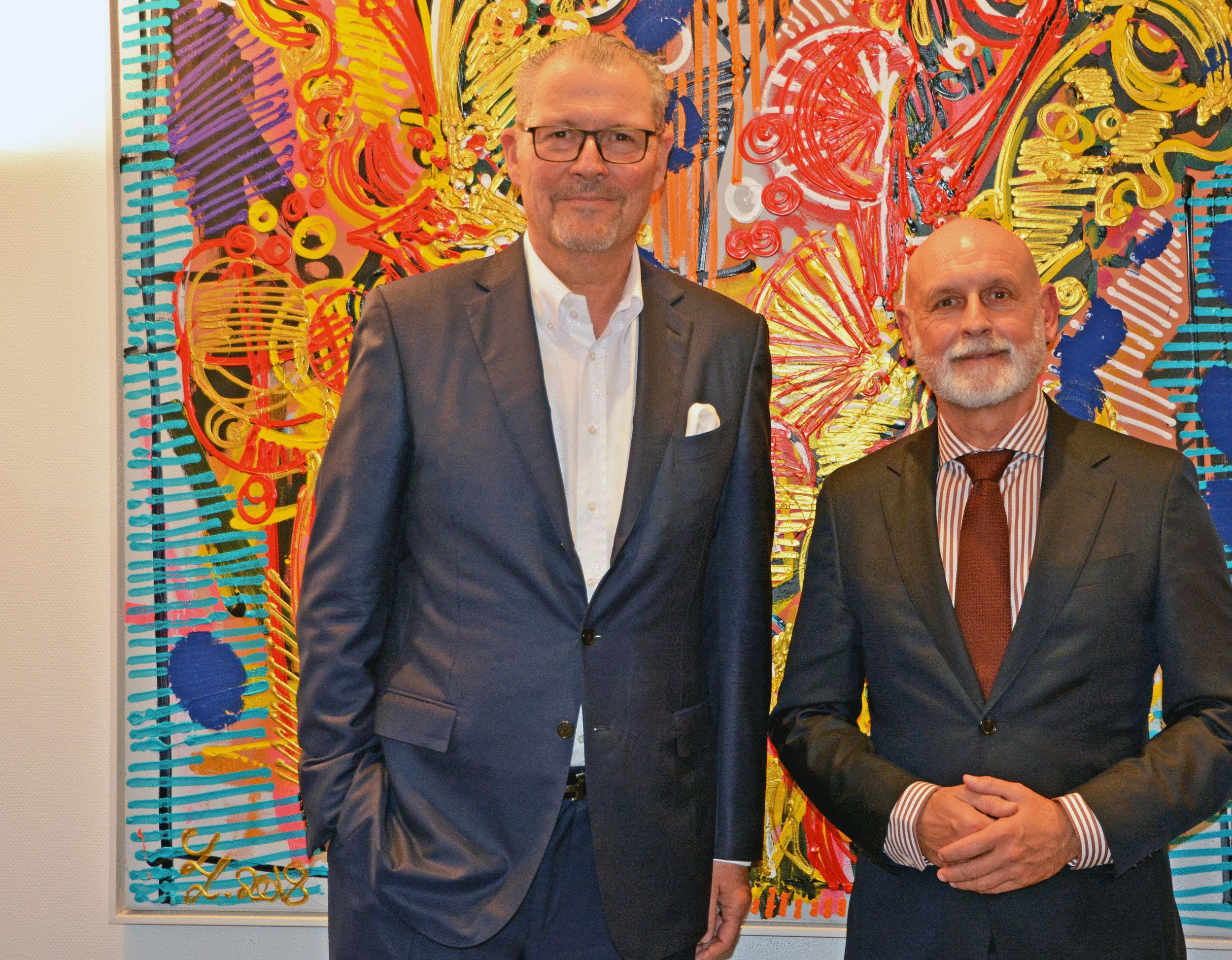 Zwei Männer in Anzügen stehen nebeneinander und schauen in die Kamera