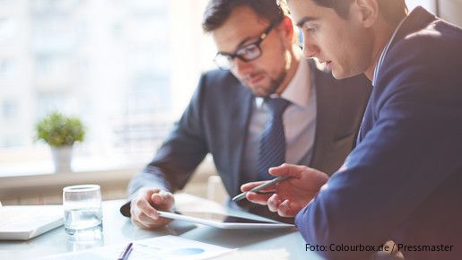 Zwei Männer im Büro sehen gemeinsam auf Tablet und besprechen sich