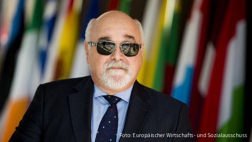Ioannis Vardakastanis im Portrait, im Hintergrund Fahnen der EU-Mitgliedstaaten