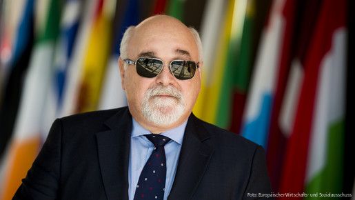 Ioannis Vardakastanis im Portrait, im Hintergrund Fahnen der EU-Mitgliedstaaten