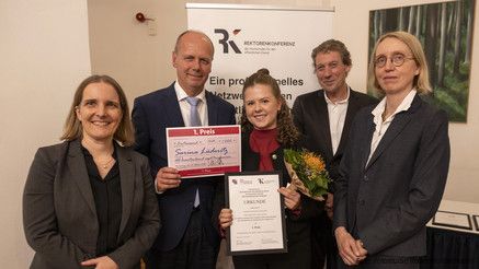Fünf Menschen halten eine Urkunde für den ersten Platz und blicken in die Kamera