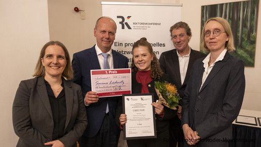 Fünf Menschen halten eine Urkunde für den ersten Platz und blicken in die Kamera