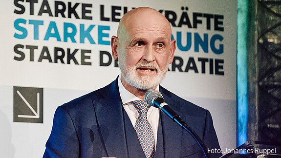 Herr Geyer steht hinter einem Rednerpult und spricht in das Mikrofon