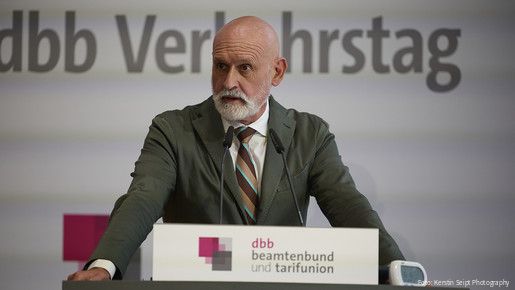 Ein Mann in Anzug steht hinter einem Rednerpult und spricht in ein Mikrofon