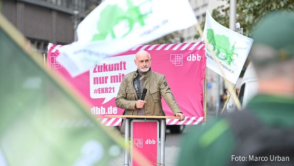 Volker Geyer Ein Mann steht im Mittelpunkt des Bildes und spricht in ein Mikrofon