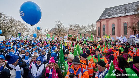 Eine Gruppe Menschen mit bunten Warnwesten und Bannern demonstriert auf einem öffentlichen Platz