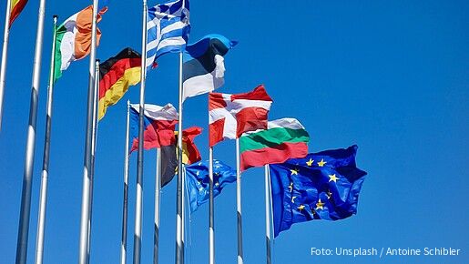 Verschiedene europäische Landesflaggen sowie eine EU-Flagge an Fahnenmasten wehen im Wind.