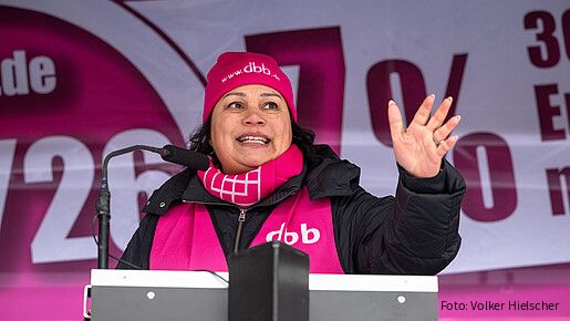 Eine Frau steht auf einer Bühne hinter einem Rednerpult und spricht in das Mikrofon