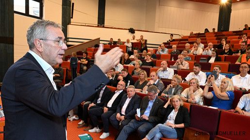 Ein Mann im Anzug spricht vor Anwesenden in einem Hörsaal