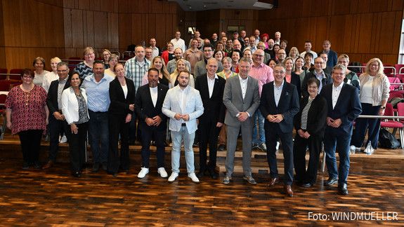 Zwei Männer und eine Frau stehen vor zwei grauen Aufstellern und blicken in die Kamera