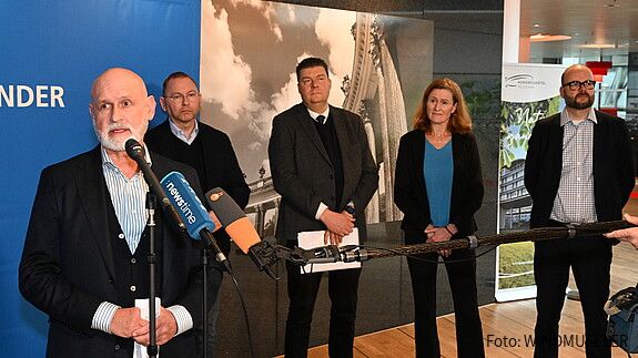 Ein Mann steht vor mehreren Mikrofonen und gibt ein Interview