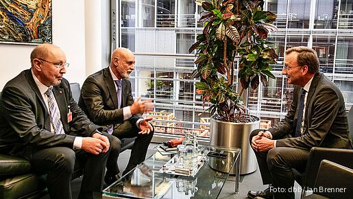 Drei Männer sitzen in einem Büro und diskutieren miteinander