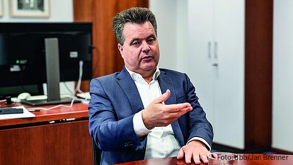 Ein Mann in Anzug sitzt an einem Tisch und gestikuliert