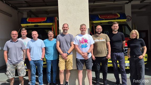 Eine Gruppe Menschen steht vor zwei Krankenwägen und schaut in die Kamera