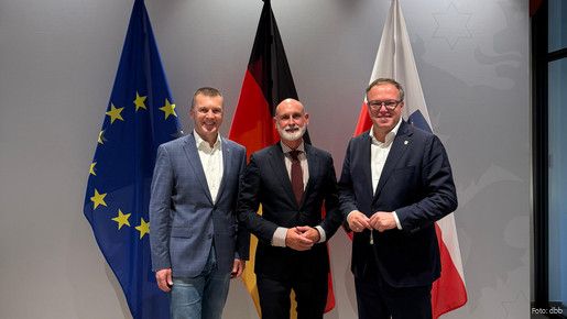 Drei Männer in Anzügen stehen vor einer EU-, Deutschland- und Thüringenflagge und blicken lächelnd in die Kamera