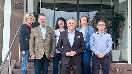 Eine Gruppe Menschen in formeller Kleidung steht auf der Treppe vor einem Gebäude