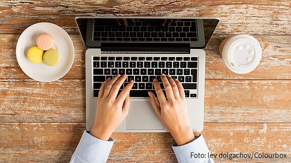 Das Foto zeigt eine Laptoptastatur, man sieht noch den Bildschirm und Finger, die auf der Tastatur tippen.